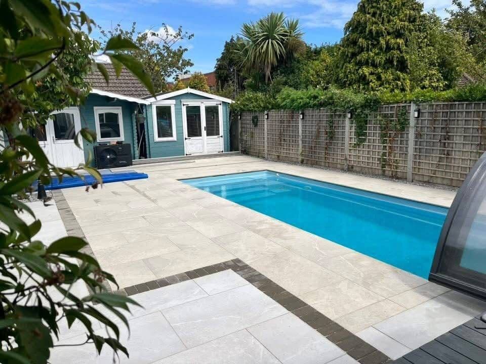 Light grey porcelain paving laid around a garden swimming pool, with a dark block border